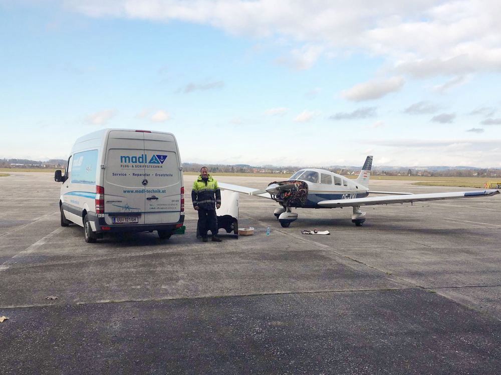 Servicewagen von Madl Flug- & Schiffstechnik neben einem einmotorigen Kleinflugzeug auf dem Vorfeld eines Flugplatzes, ein Techniker arbeitet am Fahrwerk