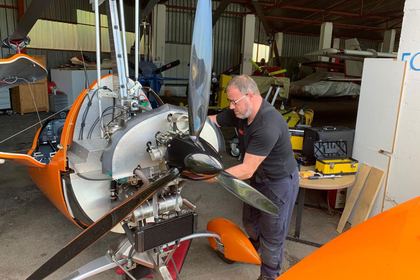 Techniker montiert den Propeller an einem orangen Tragschrauber vor der Werkstatthalle