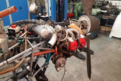 Ausgebauter Flugmotor samt Propeller und Abgasanlage auf dem Werkstattboden zur Instandsetzung