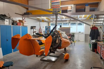 Orange lackierter Tragschrauber steht zerlegt auf der Hebebühne in der hellen Werkstatt