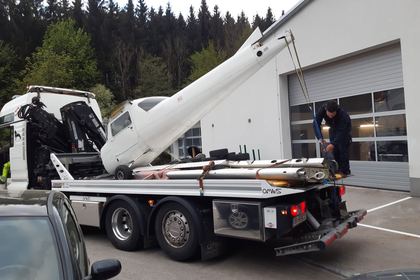Tragschrauber wird auf einem Lkw-Tieflader vor der Werkstatthalle abgeladen